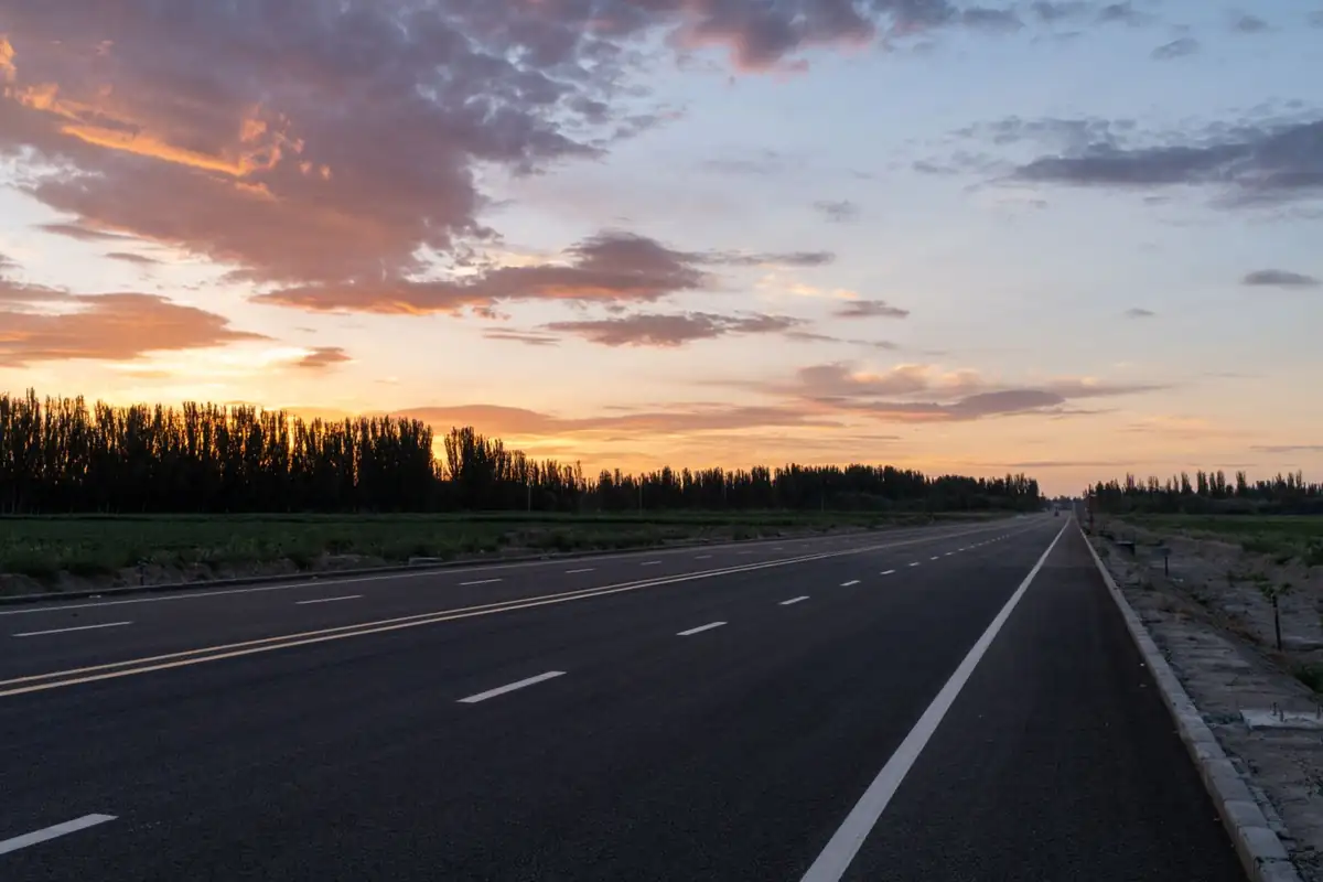 Freshly paved black asphalt road with bold yellow center lines at dusk