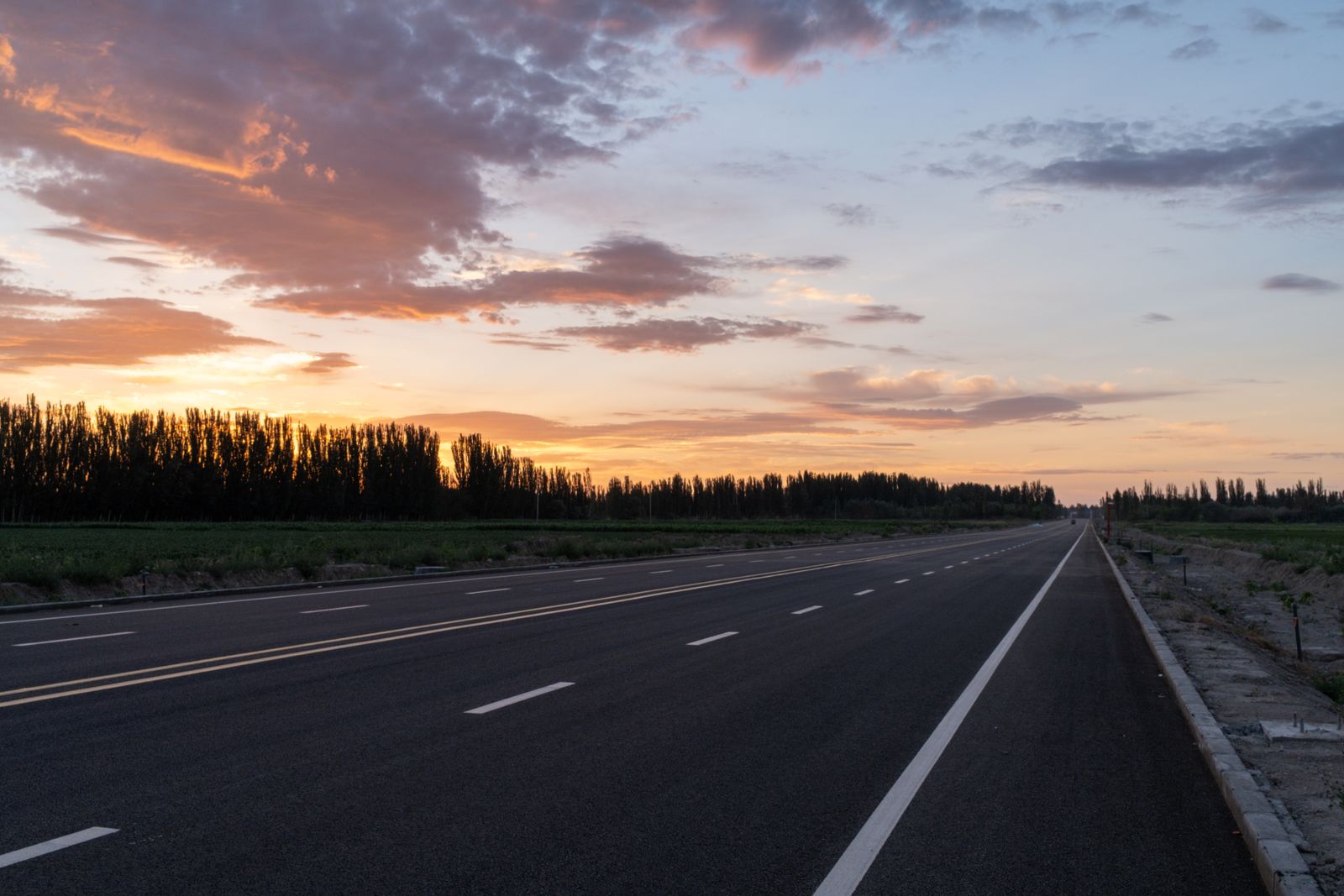 Freshly paved black asphalt road with bold yellow center lines at dusk